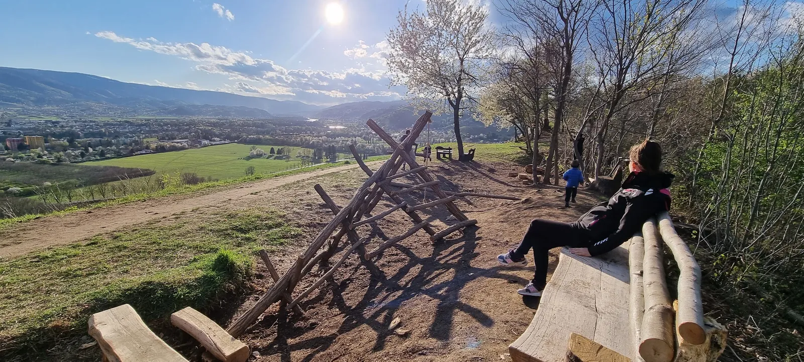 Lesena plezalna konstrukcija in klopi na vrhu Kalvarije, v ozadju razgled čez dolino proti Pohorju.